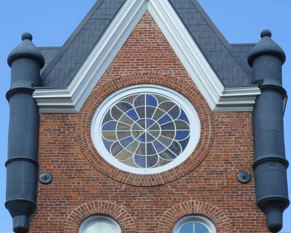 Exterior view of installed custom window. Large diameter with swooping geometric pattern and stained glass.