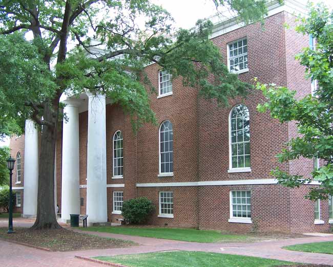 View of exterior of large brick two-story building.  There are many white-steel trimmed windows with arched tops