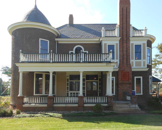 A large historic looking two-story brick home on a green lawn. White wooden windows are on all visible walls, including in round-tower section of the house.